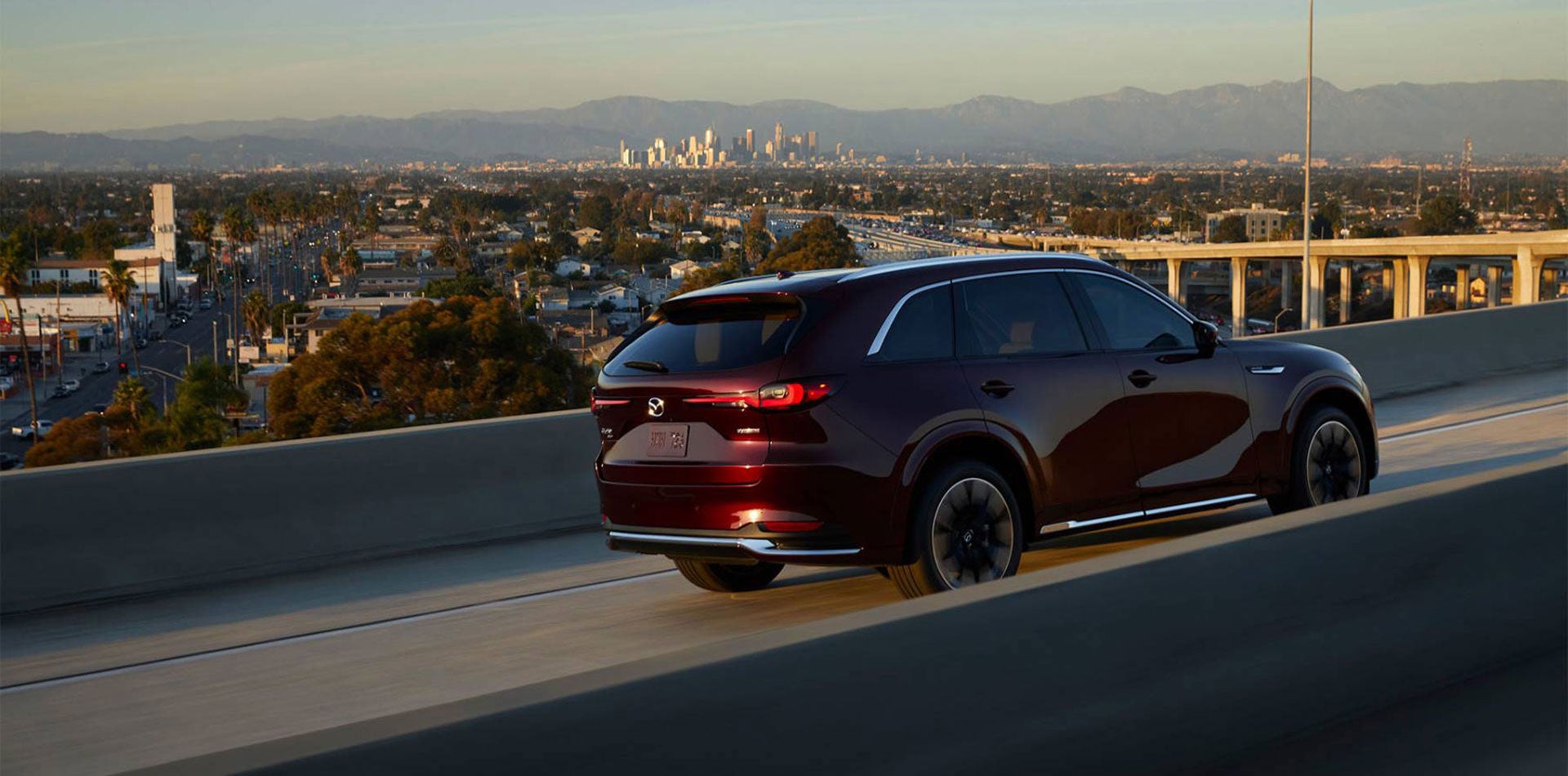 A red 2026 Mazda CX-90 SUV cruising on a flyover, highlighting its sleek design, smooth performance, and premium styling.